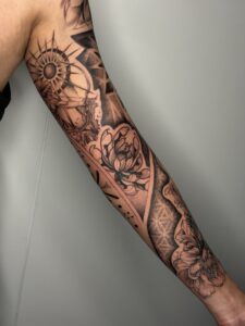 Black and grey tattoo of an archer, sun, and lotus flower on arm sleeve — 1920 Tattooz Hub, Ahmedabad