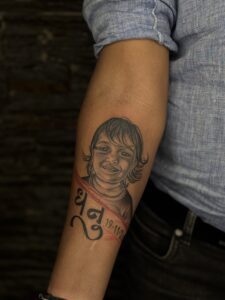 Black and grey tattoo of a child's portrait with lettering on forearm — 1920 Tattooz Hub, Ahmedabad