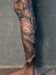 Black and grey tattoo of a dragon with cherry blossoms on calf — 1920 Tattooz Hub, Ahmedabad