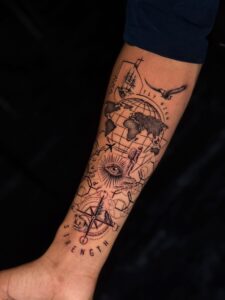 Black and grey tattoo of a globe, eagle, and travel symbols on forearm — 1920 Tattooz Hub, Ahmedabad