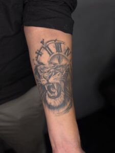 Black and grey tattoo of a roaring lion with a clock face on forearm — 1920 Tattooz Hub, Ahmedabad