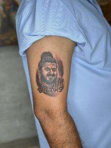 Black and grey tattoo of a man's portrait with a red bindi accent on upper arm — 1920 Tattooz Hub, Ahmedabad
