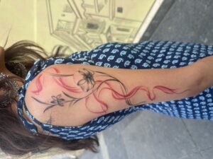 Colored tattoo of flowers with a flowing red ribbon on upper arm — 1920 Tattooz Hub, Ahmedabad
