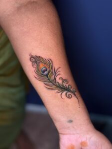 Colored tattoo of a peacock feather on forearm — 1920 Tattooz Hub, Ahmedabad