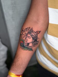 Colored tattoo of a woman's portrait with a peacock feather on forearm — 1920 Tattooz Hub, Ahmedabad