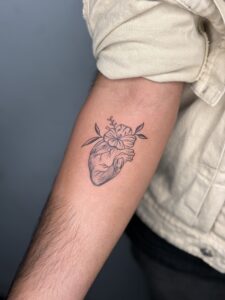 Fine line tattoo of an anatomical heart with flowers on forearm — 1920 Tattooz Hub, Ahmedabad