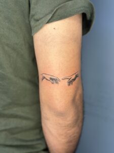 Minimalist tattoo of the Creation of Adam hands on bicep — 1920 Tattooz Hub, Ahmedabad