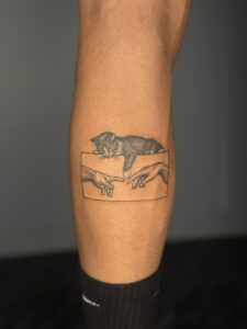 Minimalist tattoo of a kitten reaching toward the Creation of Adam hands on calf — 1920 Tattooz Hub, Ahmedabad