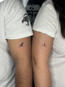 Minimalist matching tattoos of a dinosaur and a cactus on upper arms — 1920 Tattooz Hub, Ahmedabad