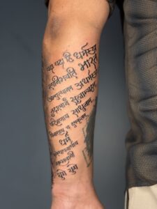 Minimalist tattoo of a Sanskrit shloka in flowing script on forearm — 1920 Tattooz Hub, Ahmedabad